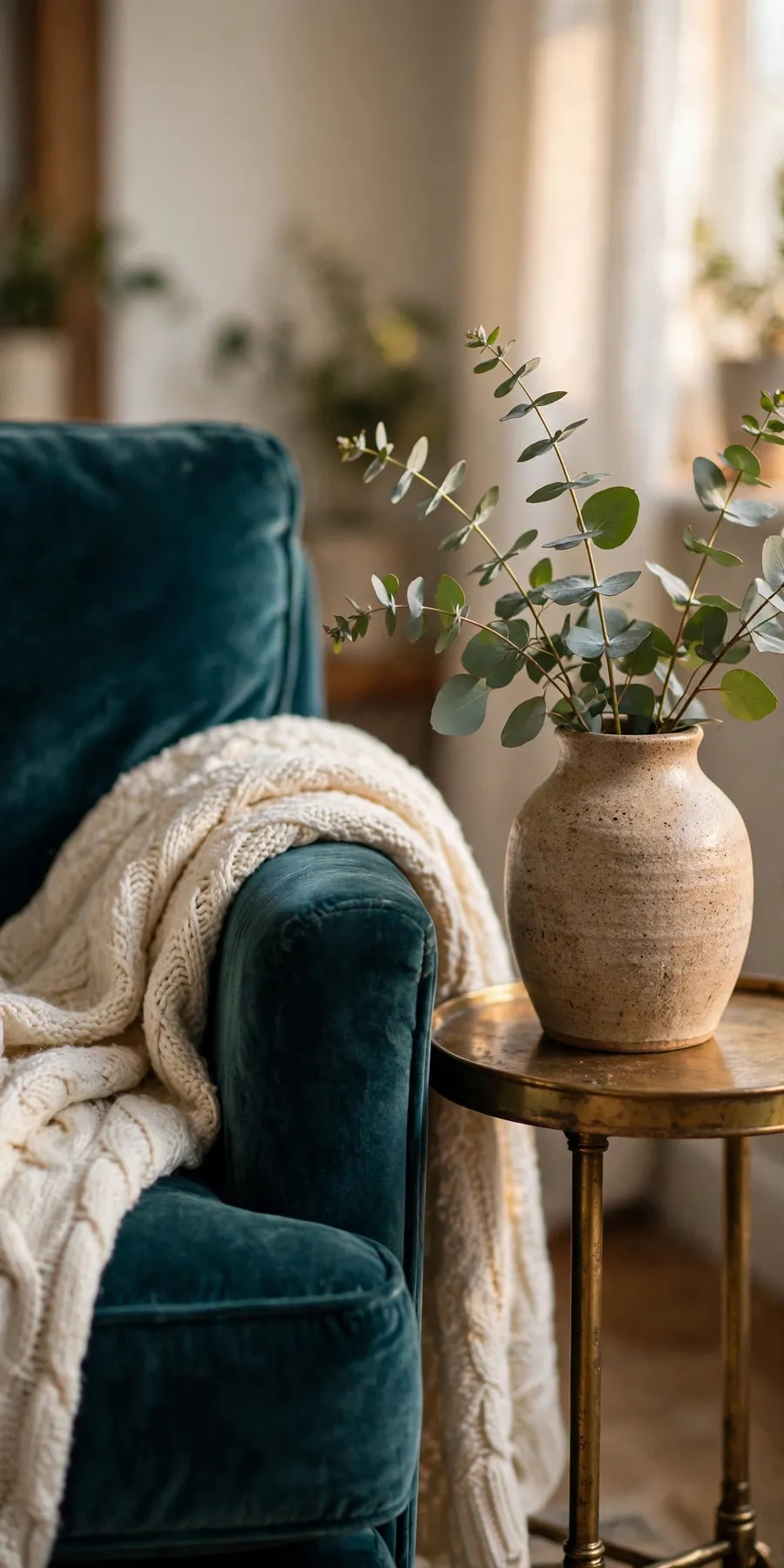 Transformative teal living room styling detail: teal velvet armchair with cream knit throw, brass side table and ceramic vase with eucalyptus